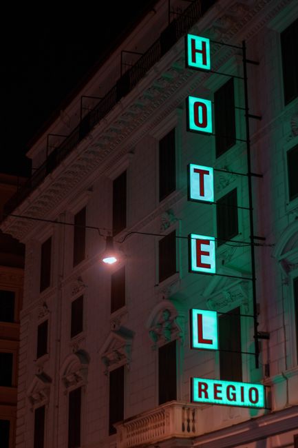 A modern hotel sign glowing brightly against a classic building in Rome, Italy at night.