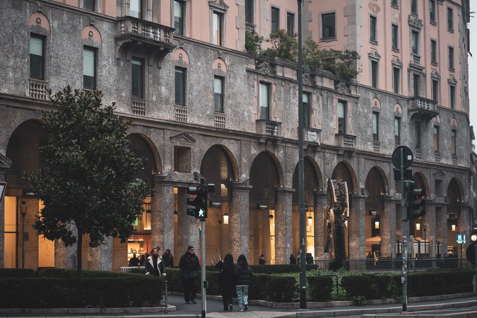 Charming historic architecture on a city street in Milan, Italy with pedestrians and lush greenery.