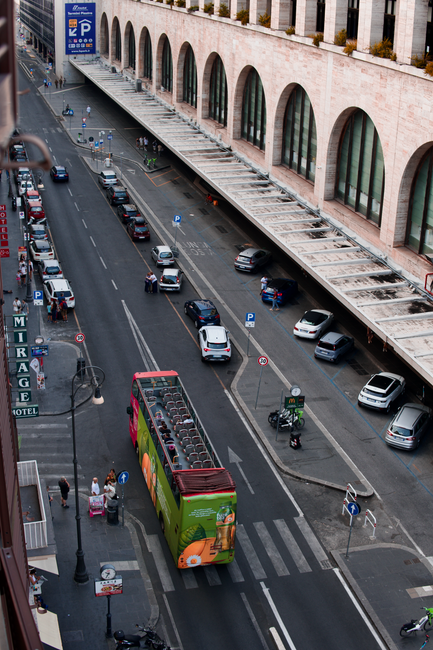 High-angle photo of a busy street in Rome featuring an open-top bus and parked cars.