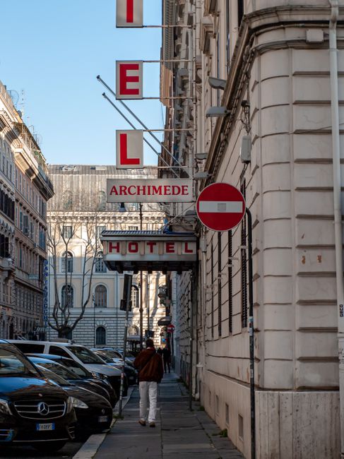 City street view showcasing Hotel Archimede with parked cars and architectural buildings.