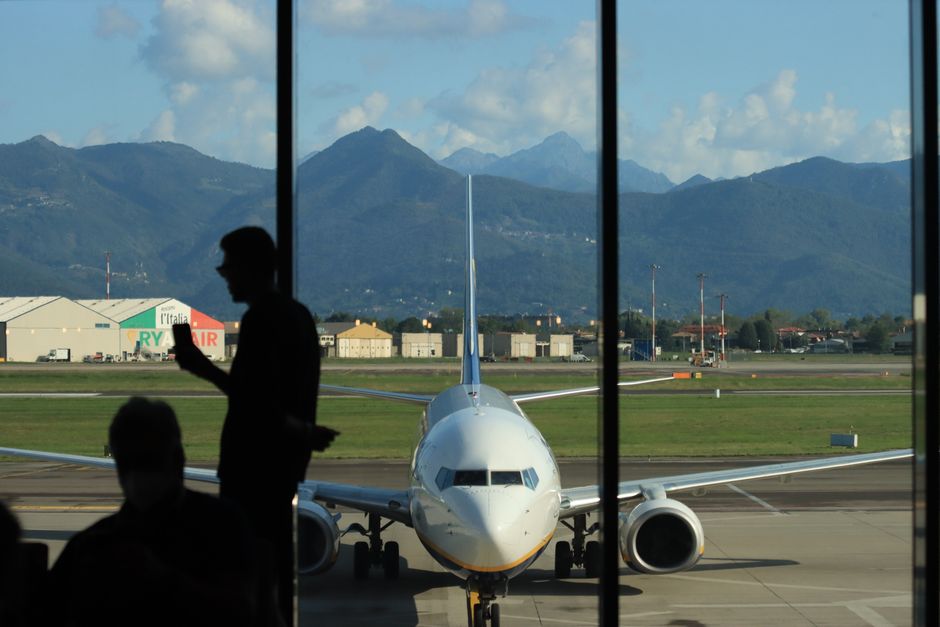 A silhouette of a person at Bergamo airport, overlooking a parked airplane with mountain backdrop.