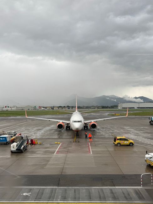 An airplane on the tarmac of an airport under cloudy skies, with airport vehicles nearby.