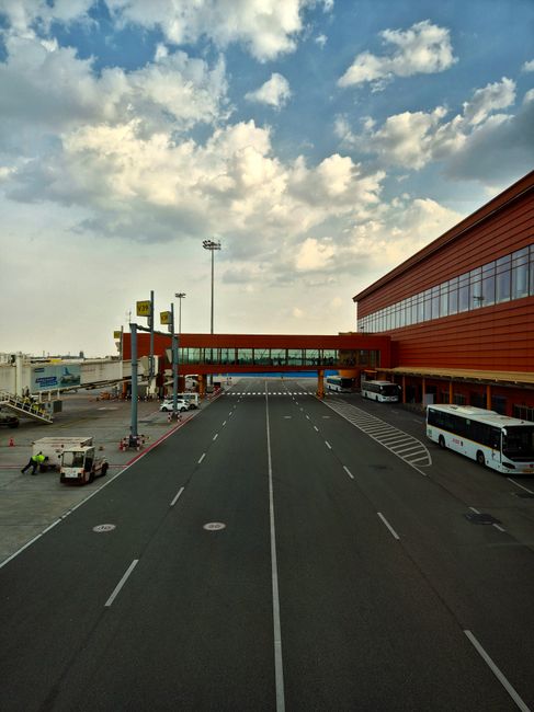 A bustling airport tarmac with terminal and buses under a cloudy sky.