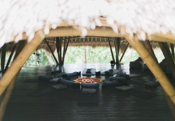 Big roof over vibrant carpet in form of flower surrounded by cushions and rubber mats on wooden floor in big gazebo
