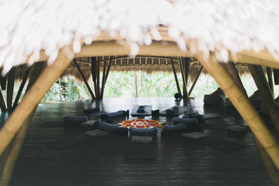 Big roof over vibrant carpet in form of flower surrounded by cushions and rubber mats on wooden floor in big gazebo