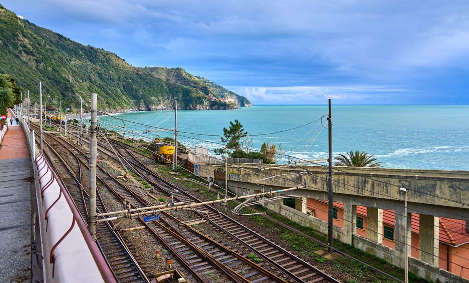 Train tracks by the Mediterranean Sea with lush hills and vivid sky.