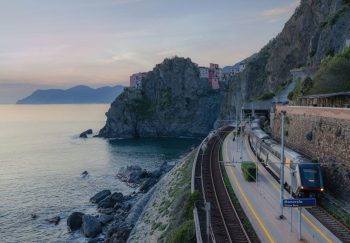 Scenic view of a train passing along cliffs near Manarola, Cinque Terre at sunset.