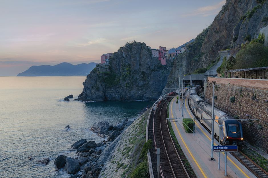 Scenic view of a train passing along cliffs near Manarola, Cinque Terre at sunset.