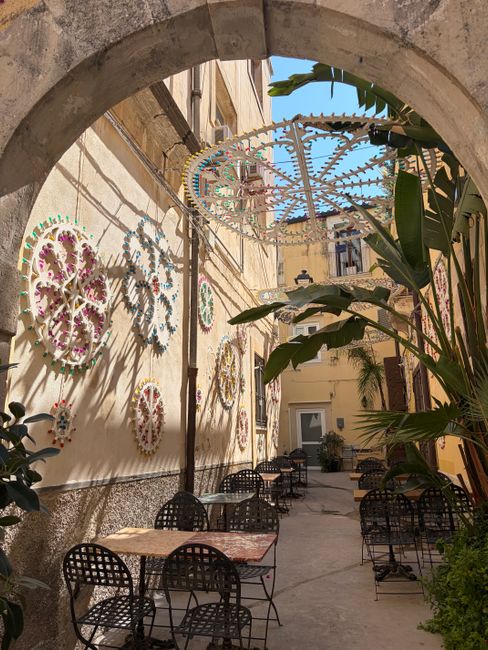 A picturesque courtyard in Syracuse, Sicily featuring decorative wall art and cozy seating.