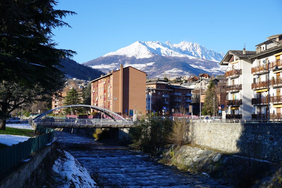 Picturesque view of a mountain town with buildings, a river, and a bridge under a clear blue sky.