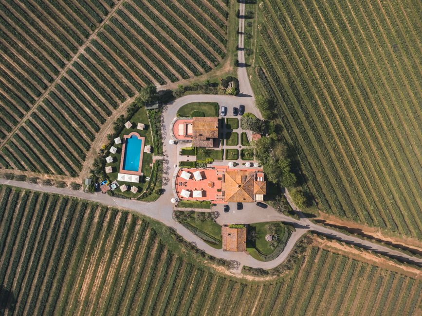 A stunning aerial shot of a traditional farmhouse with a pool and vineyards in Tuscany, Italy.