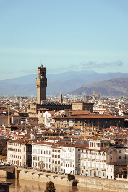 Aerial view of Palazzo Vecchio amidst Florence's historic architecture with mountains in the background.