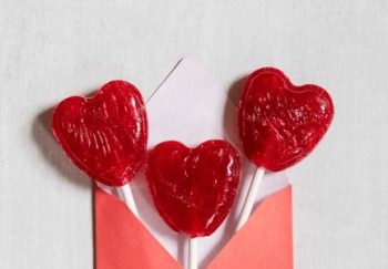 Three red heart-shaped lollipops emerge from a red envelope, perfect for Valentine's Day celebrations.