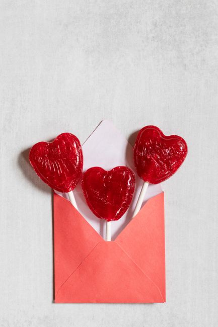 Three red heart-shaped lollipops emerge from a red envelope, perfect for Valentine's Day celebrations.