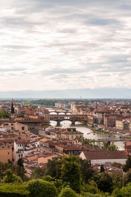 Picturesque aerial view of Florence with Arno River and historic bridges under a cloudy sky.