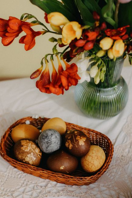 Colorful Easter eggs in a wicker basket beside a vase of vibrant flowers, perfect for spring decoration.