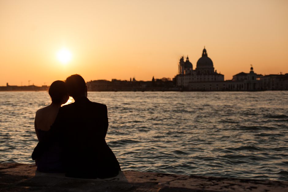 Couple silhouetted at sunset overlooking Venetian water and skyline.