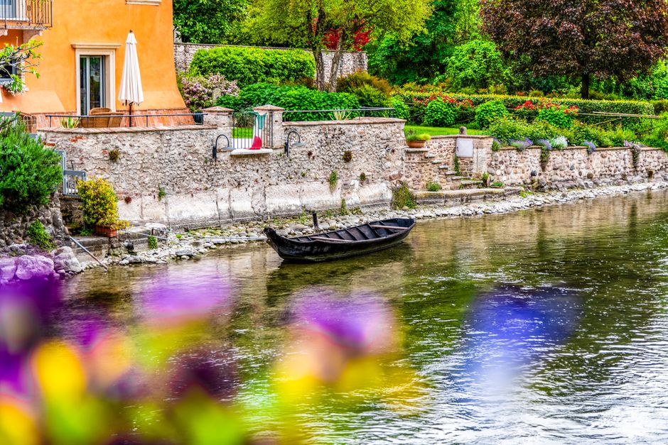 A quaint riverside view in Verona with a still boat and lush greenery, showcasing Italian charm.