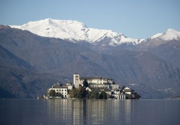 Peaceful view of Isola San Giulio and snowy Alps reflected in Lake Orta.