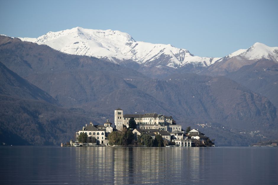Peaceful view of Isola San Giulio and snowy Alps reflected in Lake Orta.