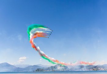 Colorful air show with jet formation flying over a lake against a clear blue sky.