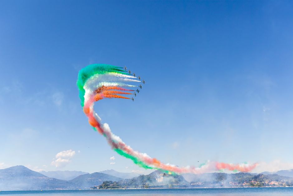 Colorful air show with jet formation flying over a lake against a clear blue sky.