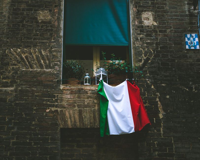 Italian flag draped outside a rustic brick building in a street setting, Italy.