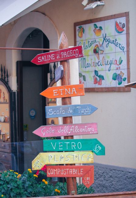 A vibrant signpost with directions to Sicilian landmarks in a charming village setting.