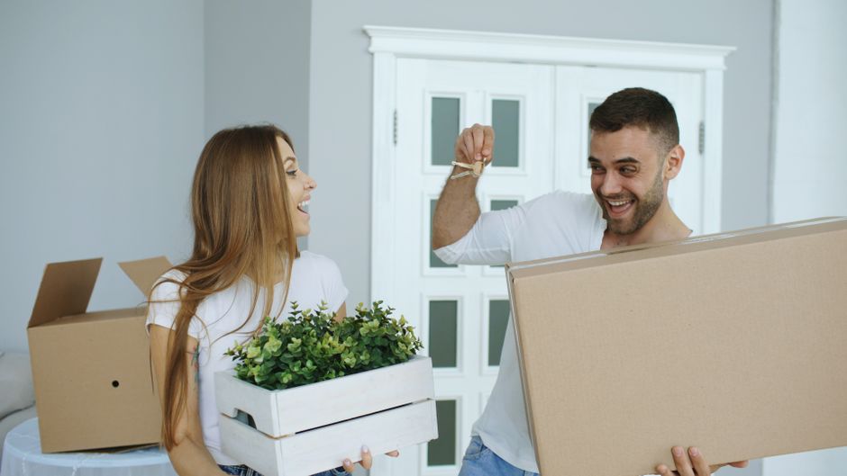 Excited couple moving into new home, unpacking boxes with plants.