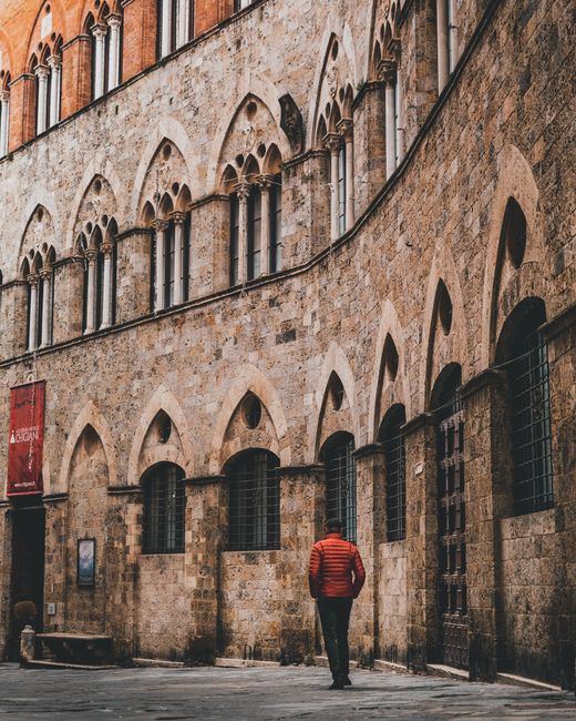 A historical building in Siena with Gothic architecture, featuring an archway and a lone person.