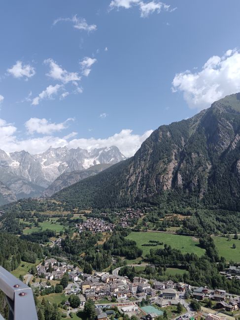 Breathtaking aerial view of Aosta Valley in Italy with lush greenery and majestic mountains under a clear sky.