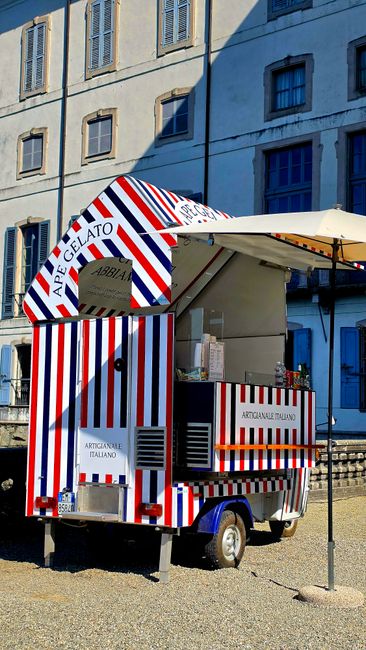A vibrant gelato cart with red, white, and blue stripes outside a European building.
