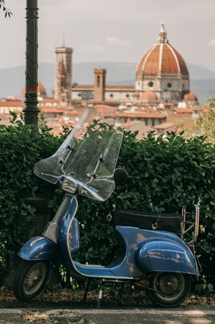 A classic blue Vespa parked with a backdrop of the Florence Cathedral in Italy.
