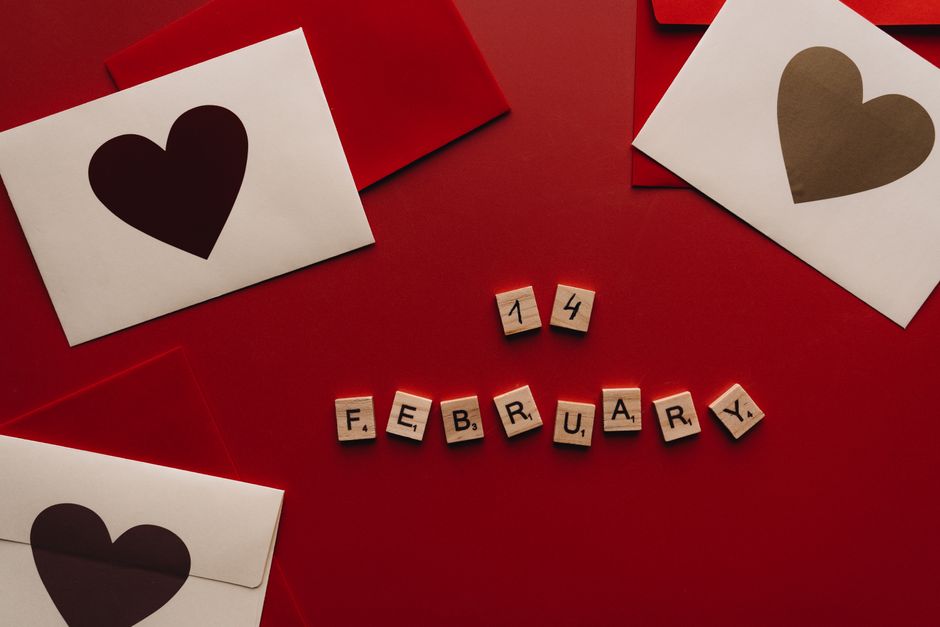 Heart-themed Valentine's Day cards and Scrabble tiles spelling February 14 on a red background.