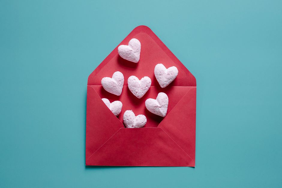 Top view of various white heart shaped decorations placed in envelope on blue background in studio during Saint Valentines day