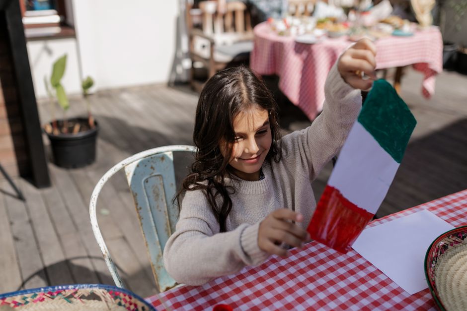 A young girl enjoys crafting an Italian flag during a festive outdoor celebration with a checkered tablecloth.