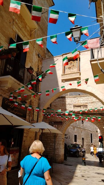Sunny day in narrow alley with Italian flags and historical architecture.