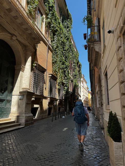 A traveler walking on a picturesque cobblestone street in Rome, Italy, surrounded by iconic architecture and greenery.